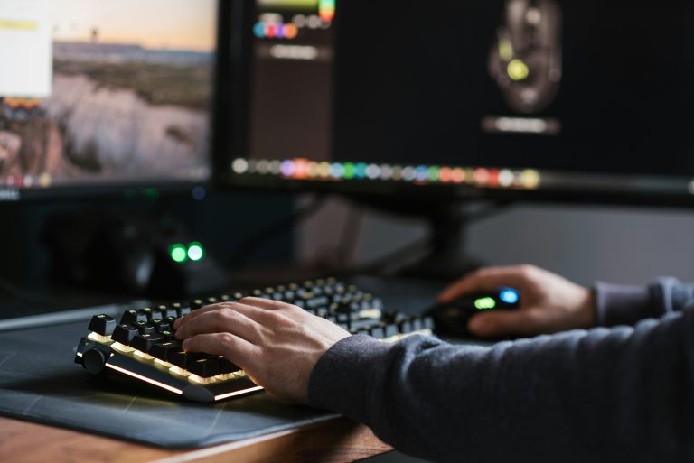 Crop anonymous male in casual outfit working on modern computer and typing on keyboard at home